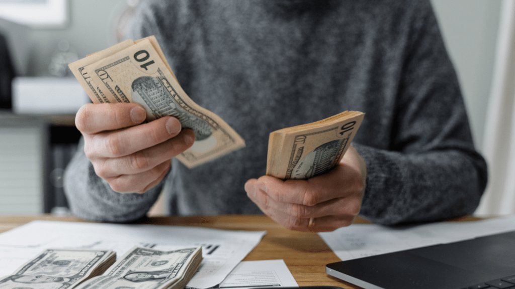 A person is counting money in front of a laptop