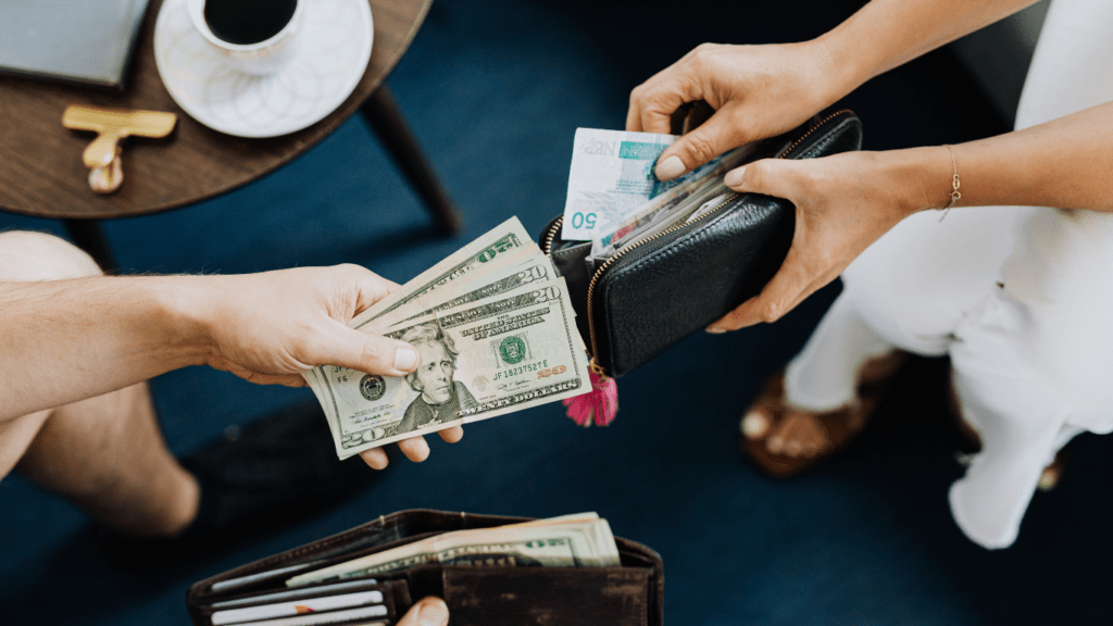 two people handing money to each other while sitting at a table