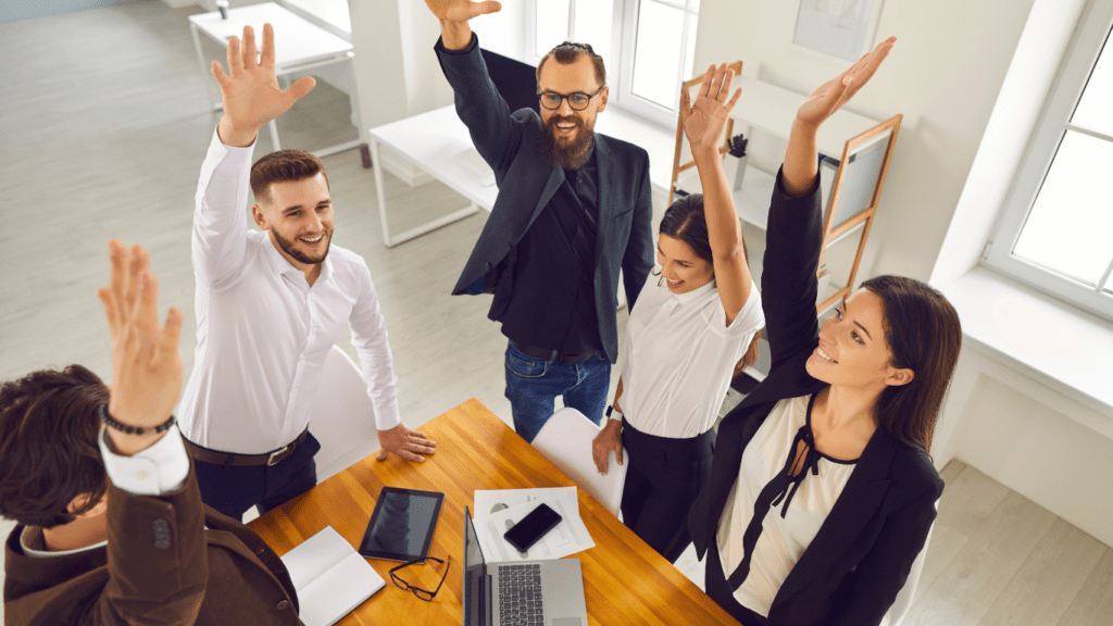 a group of people sitting around a table raising their hands